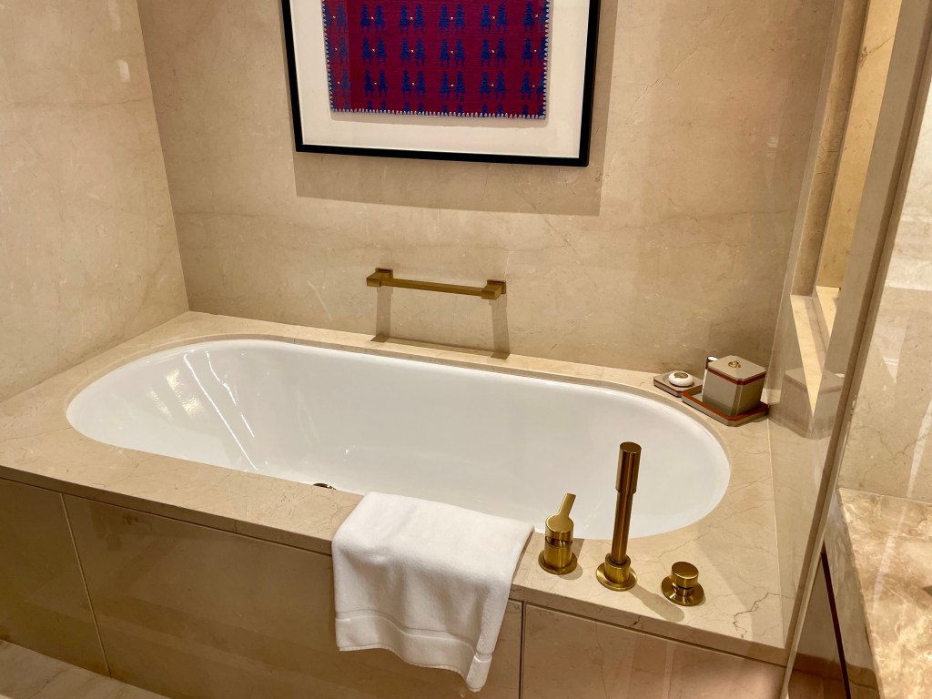 Luxury bathtub setup at Solaire Resort North, with gold fixtures, towel rack, and minimalist beige marble surroundings.