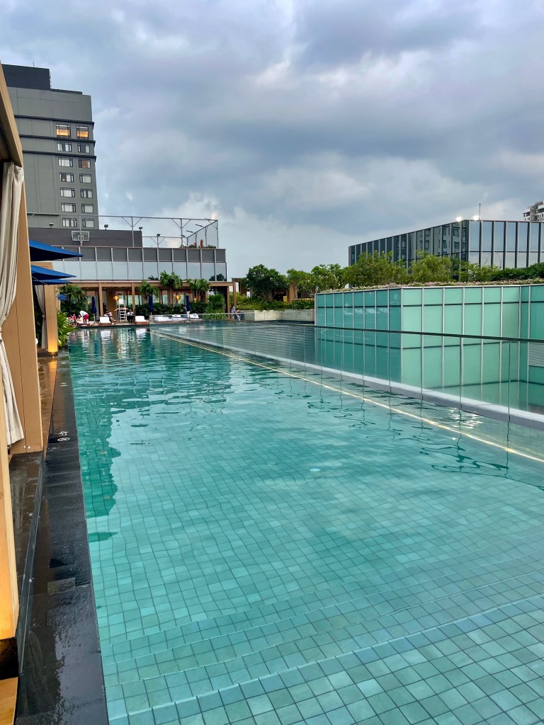 Ground-level view of the outdoor swimming pool at Solaire Resort North, designed in an L shape with clear blue water, lounge chairs, and modern architecture.